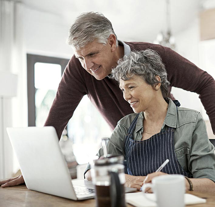 A grey-haired couple looking at a laptop at a kitchen table